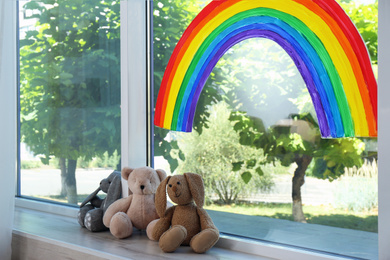 Painting of rainbow on window and toys indoors. Stay at home concept