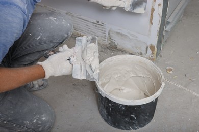 Worker plastering wall with putty knife indoors, closeup