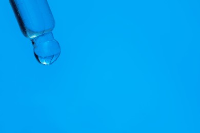 Dripping face serum from pipette on blue background, closeup. Space for text