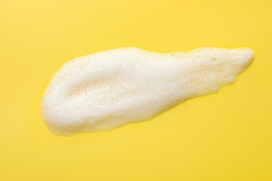 Drop of fluffy soap foam on yellow background, top view