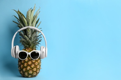 Photo of Pineapple with sunglasses and headphones on light blue background, space for text. Creative concept