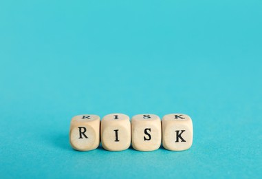Word Risk made of small wooden cubes on turquoise background