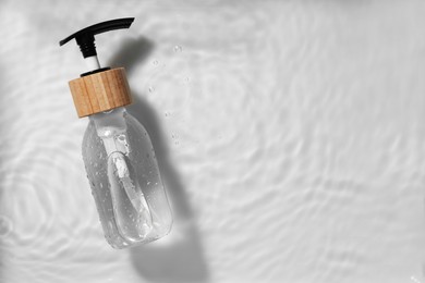 Bottle of cosmetic product in water on white background, top view. Space for text