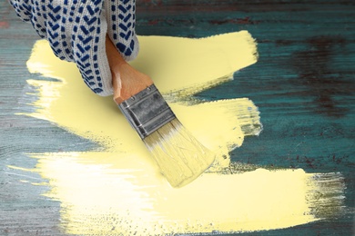 Person painting teal wooden surface yellow, closeup