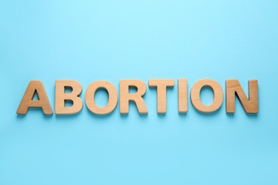 Word Abortion made of wooden letters on light blue background, flat lay