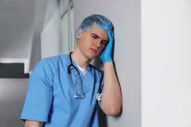 Stressed doctor near grey wall in hospital hallway