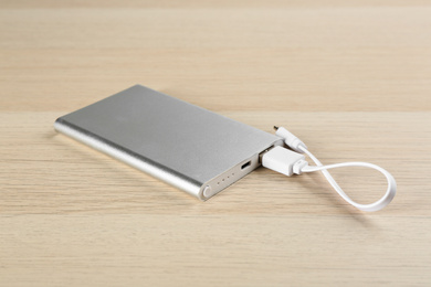 Modern portable charger with cable on wooden background