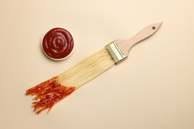 Photo of Brush painting with spaghetti dipped in ketchup on beige background, flat lay. Creative concept
