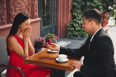 Man with engagement ring making proposal to his girlfriend in outdoor cafe