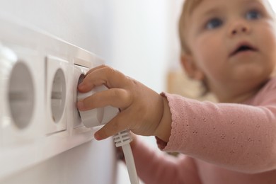 Cute baby playing with electrical socket and plug at home, focus on hand. Dangerous situation
