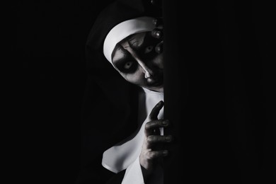 Scary devilish nun hiding on black background, space for text. Halloween party look