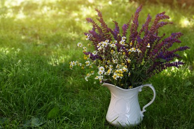 Beautiful bouquet with field flowers in jug on green grass. Space for text
