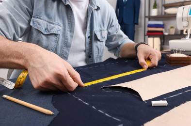 Photo of Tailor working with fabric at table in workshop, closeup