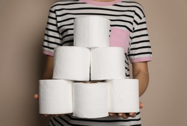 Woman with heap of toilet paper rolls on beige background, closeup