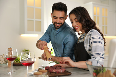 Lovely young couple cooking meat together in kitchen