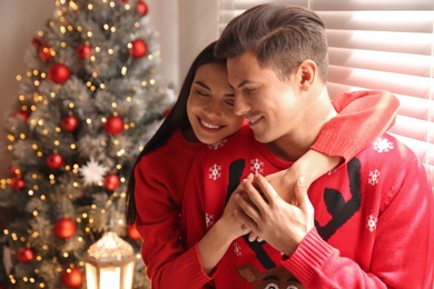 Happy couple in warm sweaters near Christmas tree indoors