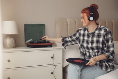 Young woman listening to music with turntable in bedroom