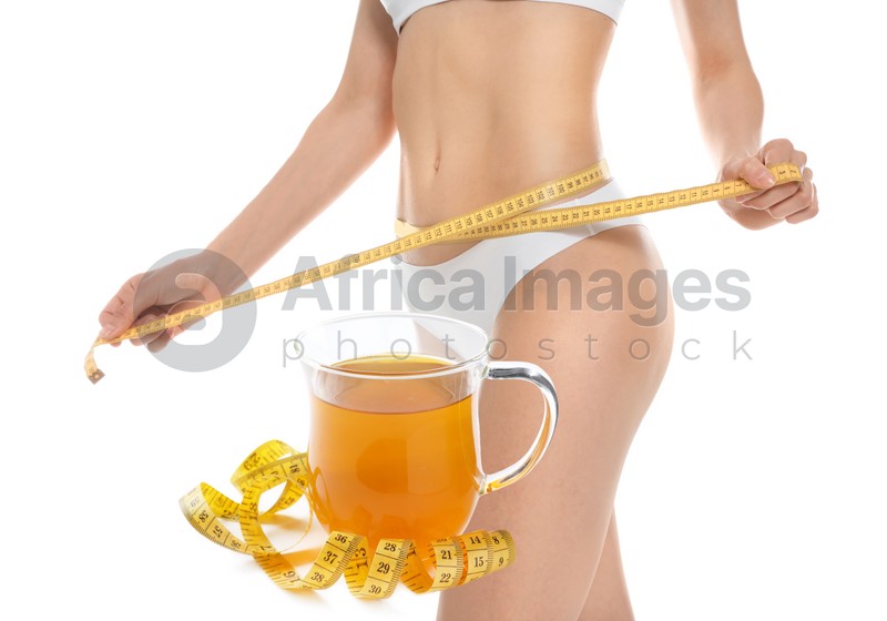 Slim young woman with measuring tape and glass cup of weight loss herbal tea on white background