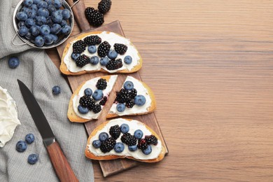 Tasty sandwiches with cream cheese, blueberries and blackberries on wooden table, flat lay. Space for text