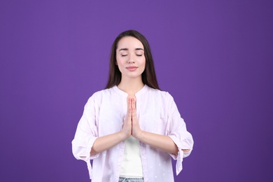 Young woman meditating on purple background. Stress relief exercise
