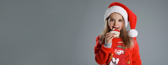 Cute little girl with Christmas gingerbread cookie on grey background, space for text. Banner design