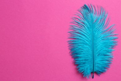 Beautiful light blue feather on pink background, top view. Space for text