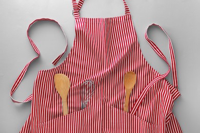 Photo of Red striped apron with kitchen tools on light grey background, top view