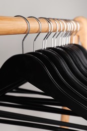 Black clothes hangers on wooden rail against light grey background, closeup