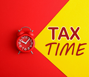 Time to pay taxes. Alarm clock on color background, top view