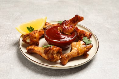Photo of Delicious fried chicken wings served with parsley, slice of lemon and sauce on light grey table