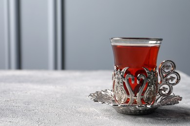 Photo of Glass of traditional Turkish tea in vintage holder on light grey table. Space for text