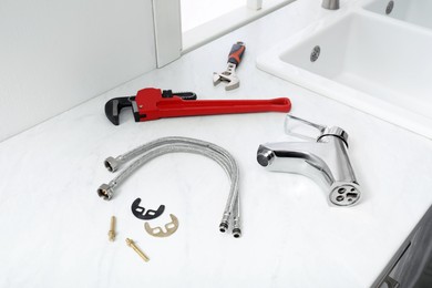Parts of water tap and wrenches on white marble countertop in kitchen