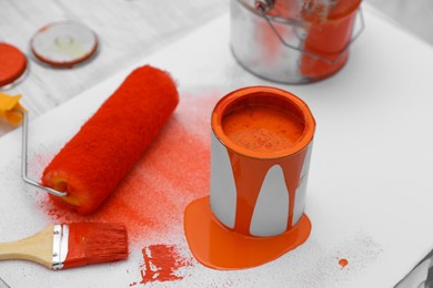 Cans of orange paint, brush and roller on white table indoors