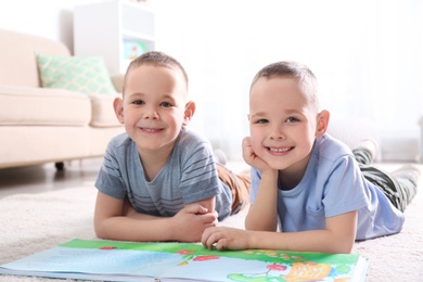 Portrait of cute twin brothers with book on floor in living room