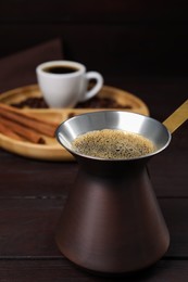 Photo of Turkish coffee pot with hot drink on wooden table