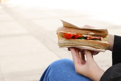 Woman holding tasty sandwich with vegetables outdoors, closeup and space for text. Street food