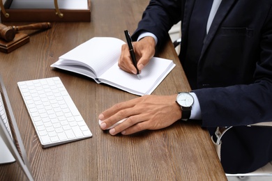 Male lawyer working with computer and notebook at table, closeup