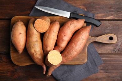 Whole and cut ripe sweet potatoes on wooden table, flat lay