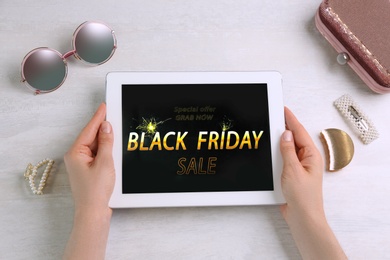 Woman using tablet with Black Friday announcement at white table, top view
