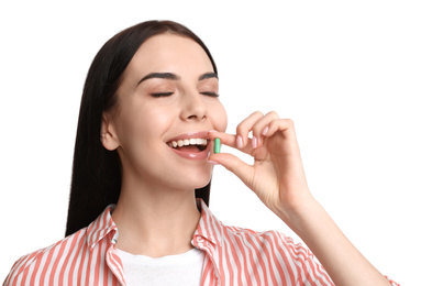 Young woman taking vitamin capsule on white background
