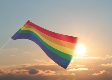 Bright rainbow LGBT flag against sky at sunrise