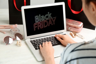 Woman using laptop with Black Friday announcement at white table, closeup