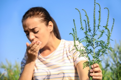 Young woman with ragweed branch suffering from allergy outdoors, focus on hand