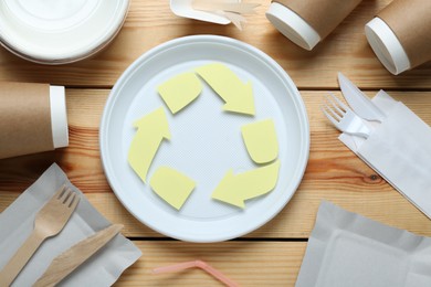 Photo of Flat lay composition with disposable dishware and recycling symbol on wooden table