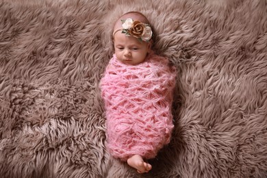 Cute newborn baby girl with floral headband lying on fuzzy rug, top view