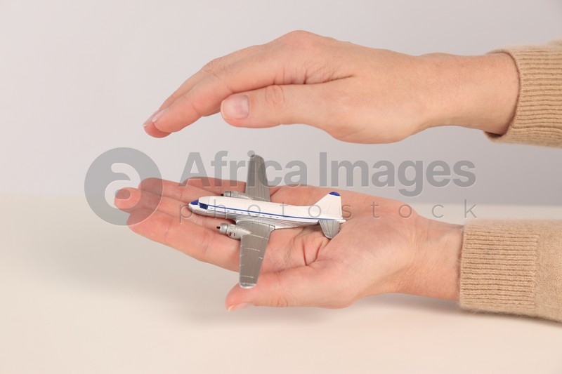 Woman covering toy plane on light background, closeup. Travel insurance concept