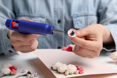 Photo of Woman using hot glue gun to make craft at white table, closeup
