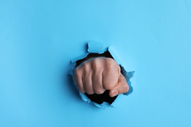 Man breaking through light blue paper with fist, closeup