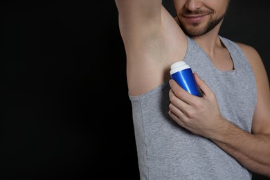 Photo of Man applying deodorant on black background, closeup. Space for text