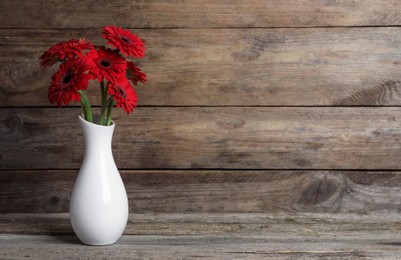 Bouquet of beautiful red gerbera flowers in ceramic vase on wooden table. Space for text